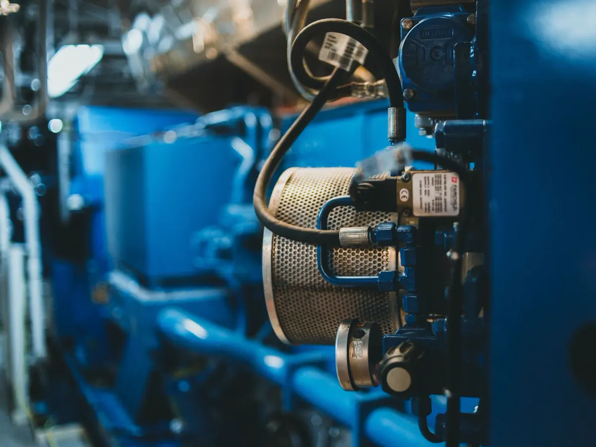 Moteur diesel de groupe électrogène en salle des machines, filtre et flexibles au premier plan.